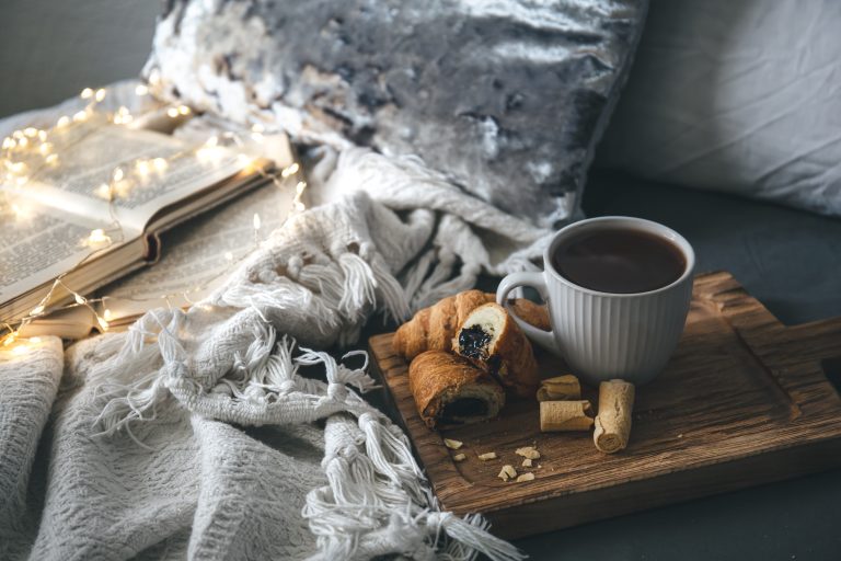 Cozy composition with a cup of tea, candles and books in bed, copy space.